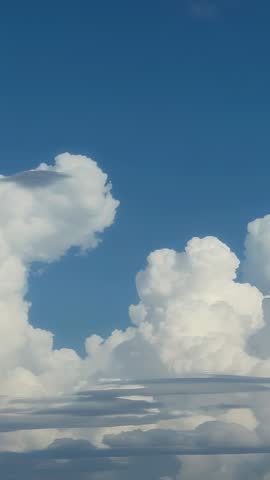 Vertical cloudscape showing towering cumulus building lenticular bases under blue sky