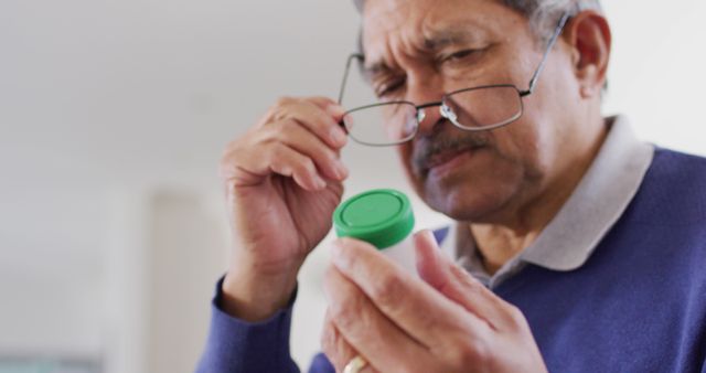 Image of serious senior biracial man looking at bottle of pills at home. Retirement, medicine, healthcare, inclusivity and senior lifestyle concept.