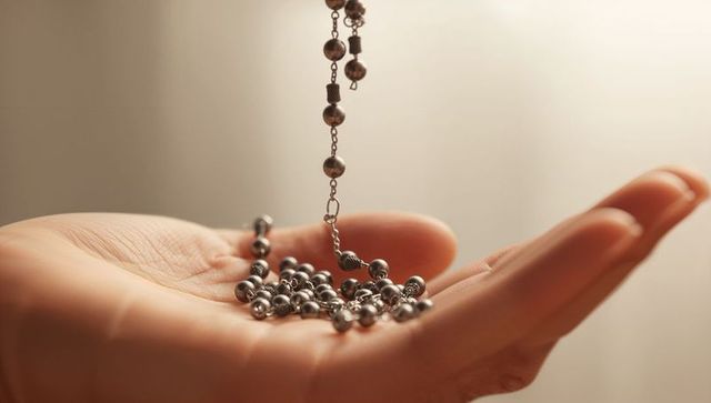Closeup of hand holding metal beaded chain showing palm lines and reflective beads
