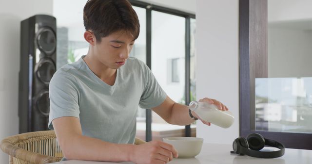 Asian male teenager sitting at table alone and having breakfast. spending time alone at home.