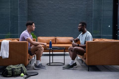 Diverse men talking in modern fitness lounge with tan leather sofas and water bottle