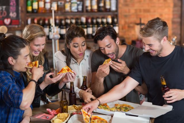 Group of friends enjoying pizza and beer in a casual restaurant setting. Perfect for illustrating social gatherings, food and beverage promotions, or lifestyle content focused on young adults having fun and bonding over meals.