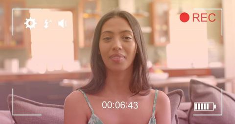 Young woman vlogging in living room with recording overlay, relaxed daylight portrait