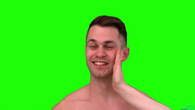 Smiling man welcoming a playful slap, generating a humorous and light-hearted vibe for the viewer. The presence of the green screen makes it perfect for use in video or digital content creation where backgrounds can be altered to suit specific themes. Use in comedic commercials, social media talks about light interactions, or collaborative projects focusing on the art of slow-motion filming.