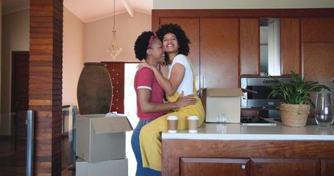 Female Couple Embracing in Kitchen Amidst Moving Boxes and Coffee Cups