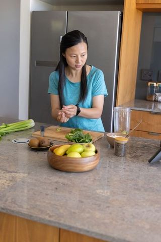 Preparing healthy green smoothie ingredients on modern kitchen island with fresh fruit