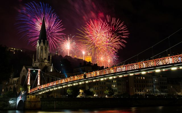 Colorful fireworks illuminating night sky above cityscape featuring prominent church and bridge. Ideal for festive, event promotion, urban celebration visuals, illuminating city vibes, captivating night scenes, holiday celebrations.