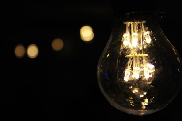 Close-up view of a glowing light bulb with a blurred bokeh background. The brightness of the filament contrasts with the dark surroundings, making the light stand out. Ideal for concepts related to electricity, illumination, and creativity. Perfect for use in presentations about energy, innovative ideas, or artistic designs involving light and shadow.