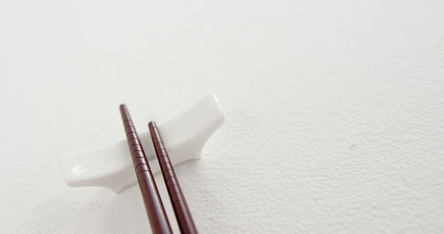 Close-up of brown chopsticks placed on a white chopstick rest on a white background. This image highlights the simplicity and elegance of traditional Japanese and Asian dining utensils. Ideal for use in publications about Asian culture, dining etiquettes, or minimalist design.