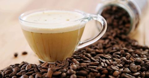 Glass cup brimming with creamy espresso foam over scattered coffee beans