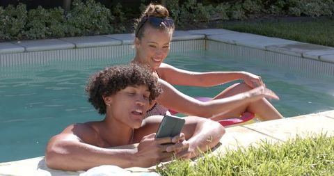 Couple enjoying summer relaxing in pool with smartphone