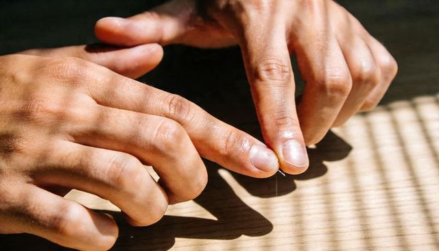 Pinching needle and thread on wooden table with striped sunlight from window blinds