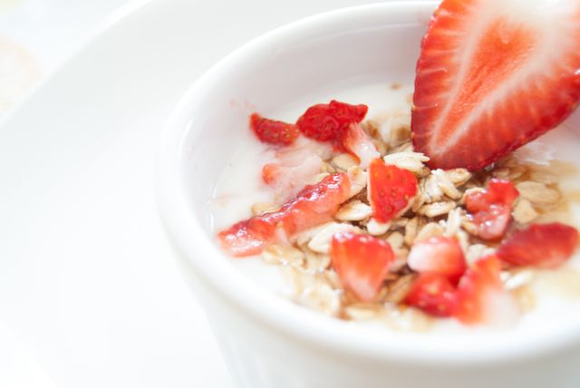 Fresh, nutritious breakfast featuring yogurt with granola topped with sliced strawberries. Perfect for food blogs, healthy eating promotions, breakfast recipes, diet meal planning, or health and wellness advertisements.