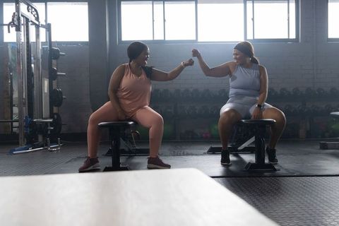 Two african american women exchanging fist bump on benches celebrating strength and teamwork