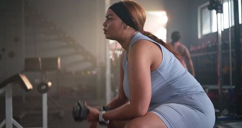 African american woman working out on bench holding dumbbell showing strength and focus