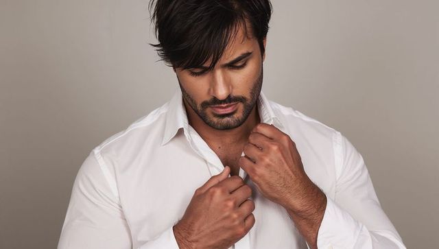 Man adjusting white shirt collar, grooming, stylish studio headshot with neutral background