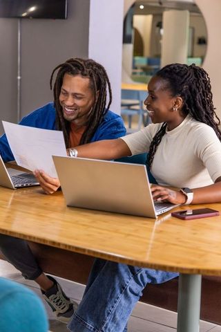 African american colleagues collaborating on documents and laptops in coworking workspace