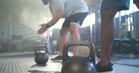 African american men preparing kettlebell lift with chalk in sunlit functional gym
