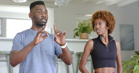 Diverse couple exercising at home with coach guiding partner by sunlit kitchen bar with plants