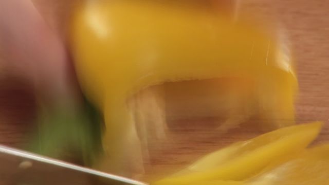 Close-up view of hands chopping a yellow bell pepper on a wooden board with a knife. The video captures the motion blur of the movement, emphasizing the action. Ideal for use in projects related to cooking, kitchen tools, recipe demonstration, food preparation videos, and culinary education materials.