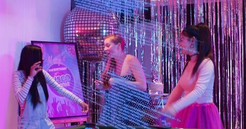 Friends dancing under disco ball at vibrant birthday party with cake