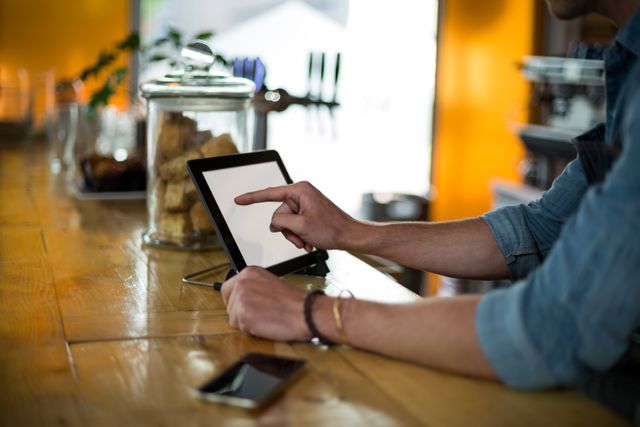 Waiter interacting with a digital tablet at a cafe counter. Ideal for illustrating modern technology in the food service industry, customer service, and digital ordering systems in cafes and restaurants.