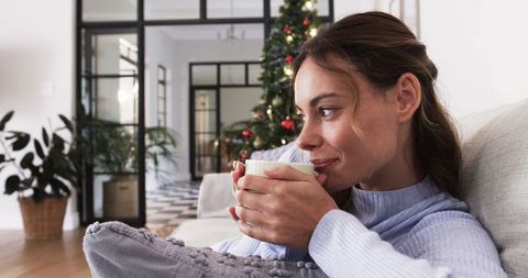 Woman Relaxing on Sofa with Mug Near Christmas Tree