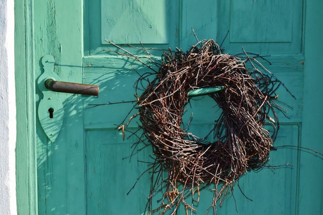 Rustic wicker wreath hanging on a vintage green wooden door. Ideal for home decor inspiration, countryside charm themes, and seasonal decoration. Perfect for holiday greeting cards, blog posts on rustic home decor, or DIY decoration ideas.