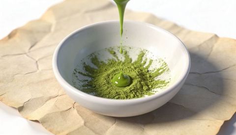 Pouring matcha paste forming glossy green droplet on powdered tea in ceramic bowl