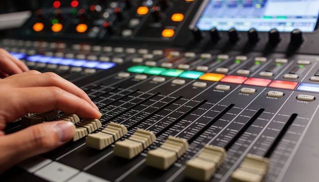 Audio engineer adjusting channel faders on professional mixing console