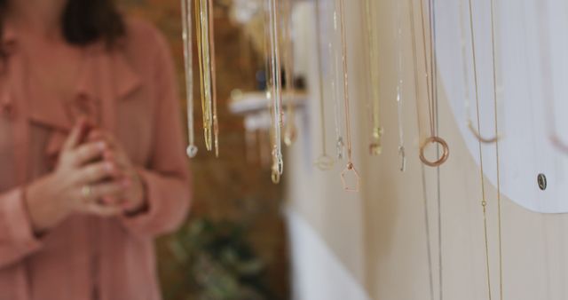 Close up of hand of caucasian woman touching golden necklaces hanging on rack, shopping for jewelry. independent handmade craft business.