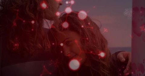 Embracing couple leaning by doorway at dusk, glowing red bokeh and floral curtain