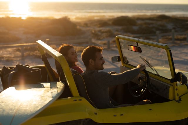 Happy caucasian couple driving beach buggy on beach at sunset, smiling. beach stop off on romantic summer holiday road trip.