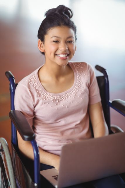 Young schoolgirl in a wheelchair smiling while using a laptop. Ideal for illustrating themes of education, inclusion, accessibility, and empowerment. Suitable for educational materials, diversity campaigns, and technology in education promotions.