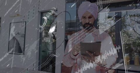 Entrepreneur wearing pink turban analyzing analytics on tablet through glass office window