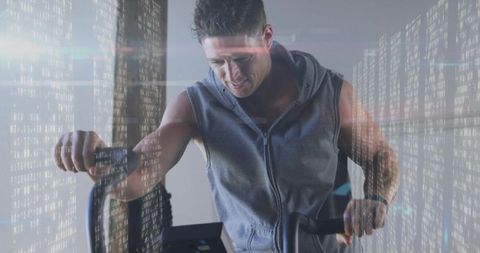 Man pedaling on exercise bike with digital overlay, sleeveless hoodie and fitness tracker