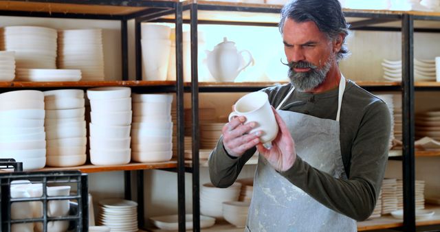Middle-aged man inspecting ceramic item in pottery workshop - Download Free Stock Images Pikwizard.com