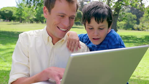 Father and Son Enjoying Laptop in Park on Sunny Day