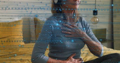 Mature woman practicing mindful breathing on yellow sofa with digital data overlay