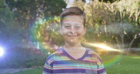 Joyful boy in striped t-shirt surrounded by rainbow lens flares outdoors