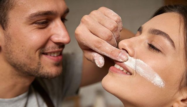 Playful couple baking in kitchen smiling man pressing flour fingertip on woman's upper lip