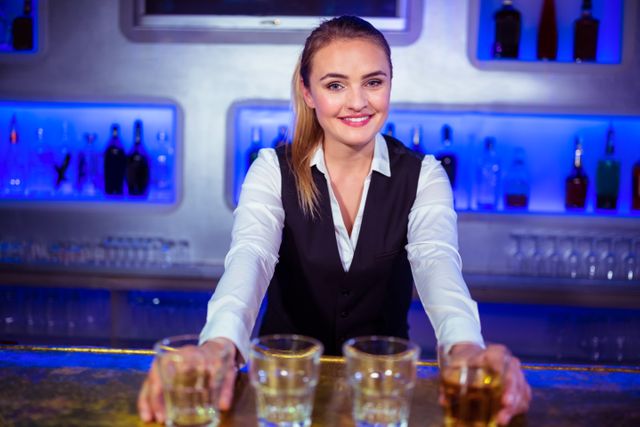 Female bartender smiling while serving drinks at a bar. Ideal for use in hospitality industry promotions, nightlife advertisements, bar and restaurant marketing materials, and customer service training resources.