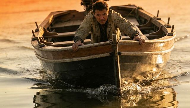 Midlife man steering wooden skiff in golden-hour water, gripping gunwale, solitary mood