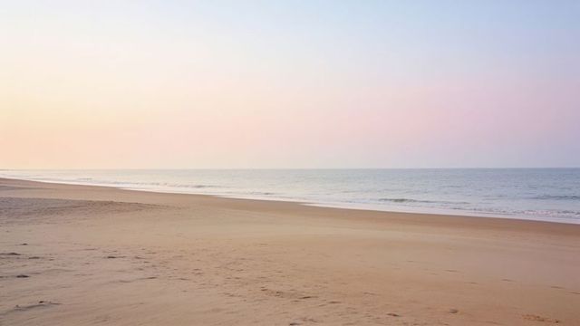 Empty sandy beach curving along calm ocean at pastel sunrise minimalist seascape