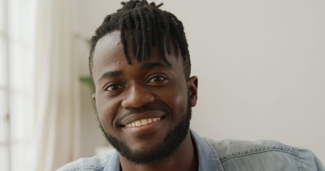 This image features a young African American man with dreadlocks smiling indoors. He wears casual clothing and exudes confidence and joy. Perfect for use in advertisements, lifestyle blogs, promotional materials, and content related to personal development, diversity, and happiness.