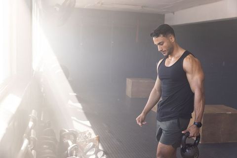 Muscular man holding kettlebell in sunlit gym near plyometric boxes showcasing strength