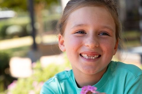 Smiling young girl holding pink flower in garden closeup portrait with freckles