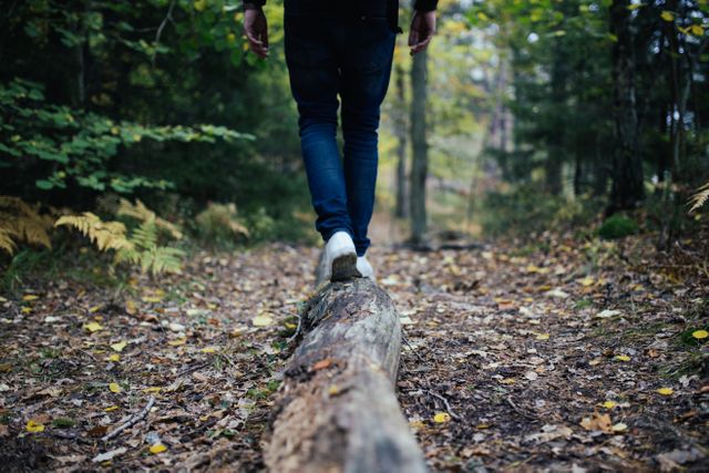 Individual navigating a forest path, carefully balancing on a log with lush greenery and fallen leaves around. Ideal for travel, adventure, and nature-related content showcasing serenity and outdoor activities.