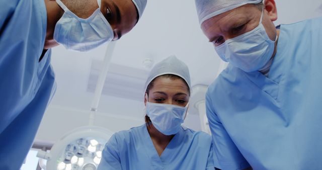 Group of surgeons wearing masks and scrubs, focusing intently on a surgical procedure. Perfect for illustrating medical teamwork, healthcare services, and the seriousness of surgical operations. Ideal for use in medical articles, healthcare-related promotions, and educational materials.