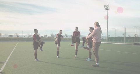 Female team stretching on synthetic turf with coach leading warmup in golden light